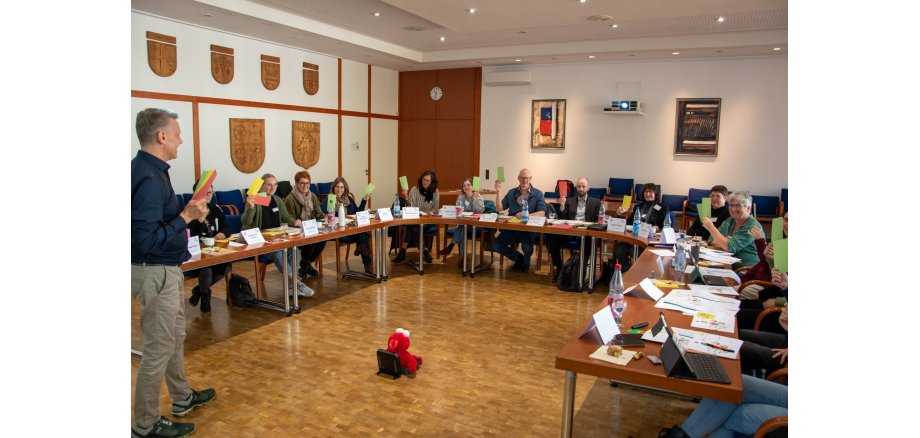 Auf dem Bild erkennt man eine Vielzahl von Personen, die in einer "Hufeisen-Formation" sitzen. Im Vordergrund steht ein Dozent.