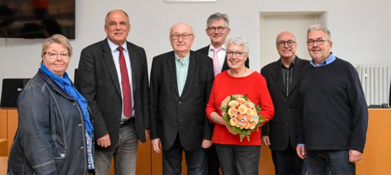 Auf dem Bild sieht man eine Gruppe von sieben Personen, die in einem Gerichtssaal stehen.