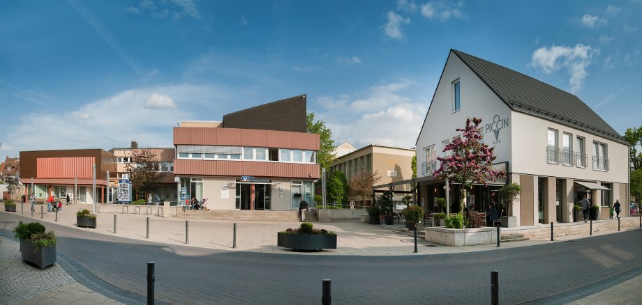 Auf dem Foto erkennt man den Rathausplatz von Nieder-Olm. Links das Rathaus, in der Mitte eine Volksbankfiliale und rechts ein Eiscafé.