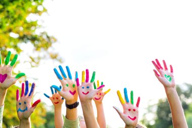 Auf dem Bild erkennt man Kinderhände. Diese sind bunt bemalt und man erkennt mehrere lachende Gesichter.